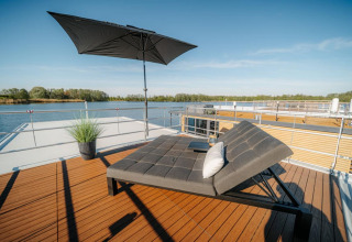 Terrazza soleggiata su una houseboat a Zehdenick con lettino moderno, ombrellone e vista sull’acqua.