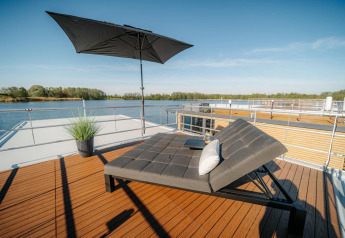 Terrazza soleggiata su una houseboat a Zehdenick con lettino moderno, ombrellone e vista sull’acqua.