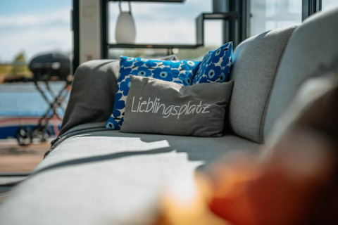 Gray sofa with blue floral pillows and a pillow with 'Lieblingsplatz' on a houseboat in Zehdenick.