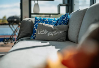 Divano grigio con cuscini blu e uno con la scritta 'Lieblingsplatz' su una houseboat a Zehdenick.