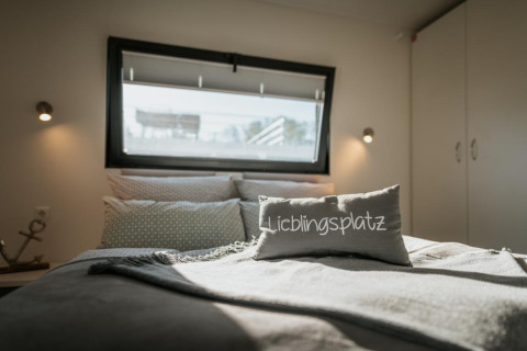 Camera da letto su una houseboat a Zehdenick con cuscino 'Lieblingsplatz' e luce soffusa dalla finestra.
