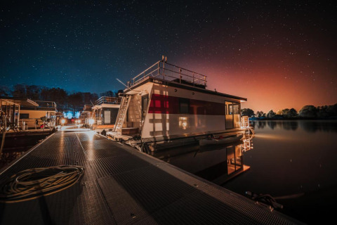 Starry night over a houseboat docked in Zehdenick, Germany, with serene water and glowing lights.