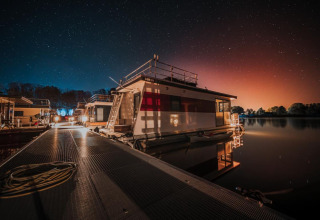 Notte stellata su una houseboat attraccata a Zehdenick, Germania, con acqua tranquilla e luci calde.