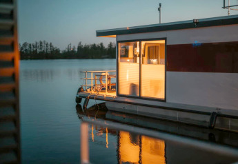 Verlichte woonboot op rustig water bij valavond in Zehdenick, met bomen en waterreflecties zichtbaar.