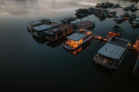 Aerial view of houseboats at Houseboat in Zehdenick, some warmly lit and floating peacefully at dusk.