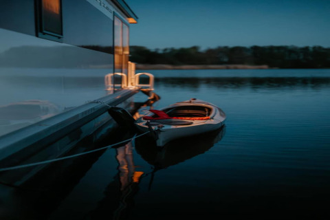 Kayak tied to a houseboat on calm water at dusk, peaceful scene from Houseboat in Zehdenick.