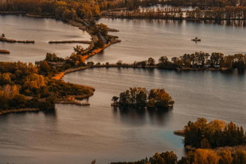 Aerial view of islands and a houseboat in Zehdenick, surrounded by autumn-colored trees and calm waters.