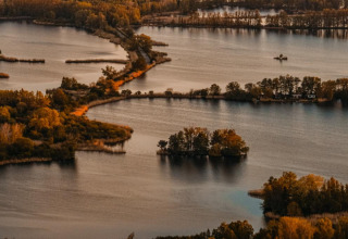 Vista aerea di isole e una houseboat a Zehdenick, circondata da alberi in colori autunnali e acque calme.