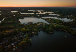 Foto aérea al atardecer de una casa flotante en Zehdenick, Alemania, rodeada de ríos y bosques verdes.
