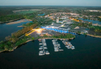 Luchtfoto van een woonboot en jachthaven in Zehdenick bij zonsondergang, omgeven door bos en dorp.