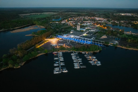 Aerial view of a houseboat and marina in Zehdenick at dusk with surrounding forest and a town nearby.