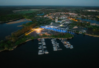 Vista aerea di una houseboat e marina a Zehdenick al tramonto, circondate da foresta e una città vicina.