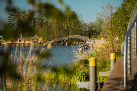 Riverside view with a bridge, dock, and lush greenery near Houseboat in Zehdenick on a sunny day.