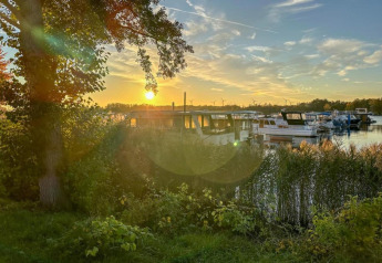 Coucher de soleil sur une péniche à Zehdenick, arbres et roseaux devant, eau calme à l’arrière-plan.