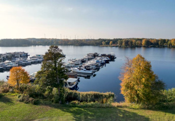 Udsigt over havn med husbåde og både ved sø i Zehdenick, omgivet af træer i efterårsfarver.
