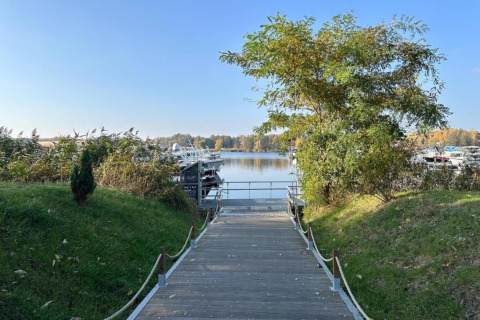 Un sentiero di legno porta alle houseboat sull'acqua a Zehdenick, circondate da alberi verdi.
