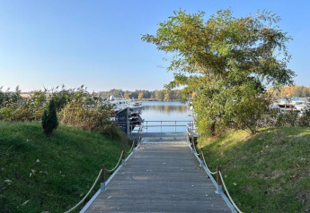 Un sendero de madera conduce a casas flotantes en el agua en Houseboat en Zehdenick, rodeado de árboles verdes.