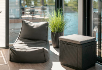 Modernes Lounge-Bereich auf einem Hausboot in Zehdenick mit Sitzsack, Hocker und Pflanze am Fenster.