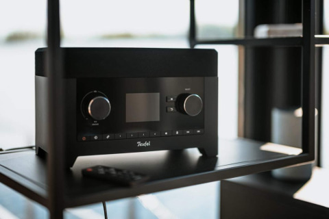 Black Teufel radio with remote on a shelf inside a modern houseboat in Zehdenick, large window view.