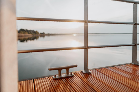 Vista dalla Houseboat am Gräbendorfer See con ponte in legno, corrimano e riflesso del sole sul lago.