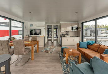 Sala y cocina moderna en una casa flotante en Zehdenick con ventanales, mesa de comedor y sofá cómodo.