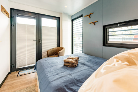 Camera da letto su una houseboat a Zehdenick con letto matrimoniale, copriletto blu e finestre moderne.