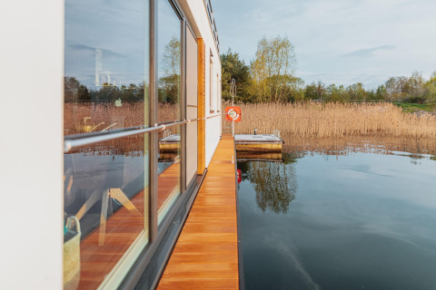 Flot udsigt fra Houseboat am Gräbendorfer See med træterrasse, spejlklare sø og siv omgivet af natur.