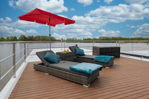 Sun deck on Houseboat in Zehdenick with loungers, red umbrella, and scenic water and nature view.