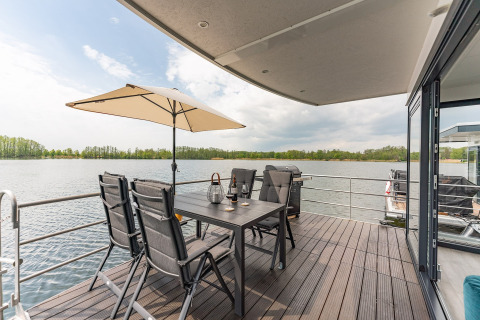 Udsigt fra terrasse på husbåd i Zehdenick med spisebord, stole, parasol og udsigt over søen.