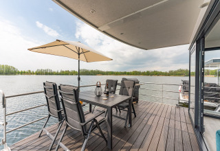 Terrazza di una houseboat a Zehdenick con tavolo, sedie, ombrellone e vista panoramica sul lago.