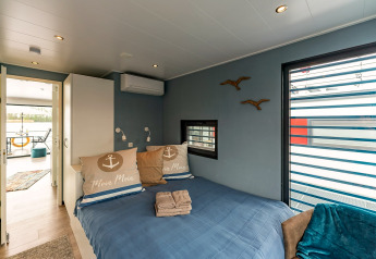 Schlafzimmer auf einem Hausboot in Zehdenick mit Doppelbett, Fenster und Blick zur Terrasse.
