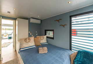 Slaapkamer op een woonboot in Zehdenick met tweepersoonsbed, blauwe muren en zicht op terras.