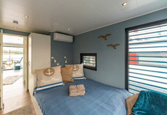 Chambre sur une péniche à Zehdenick avec lit double, murs bleus, fenêtre et vue sur la terrasse.