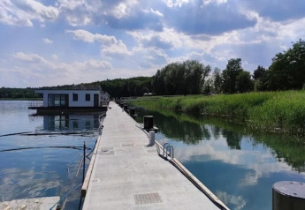 Een moderne woonboot aan het Gräbendorfer See, aangemeerd aan een betonnen steiger langs het riet.