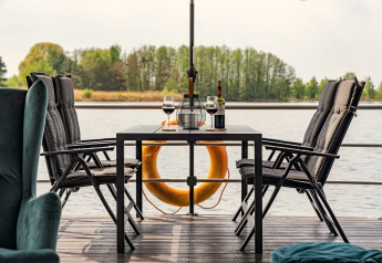 Esstisch mit Wein und Gläsern auf einem Hausboot in Zehdenick, mit Blick aufs Wasser und Bäume.