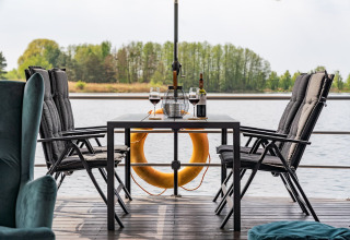 Mesa con vino y copas en una casa flotante en Zehdenick, vista al agua y árboles alrededor.