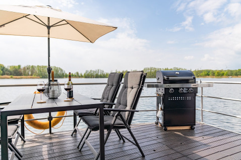 Zona de comedor al aire libre en una casa flotante en Zehdenick, Alemania, con parrilla y vista al lago