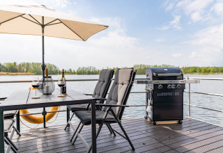 Zona de comedor al aire libre en una casa flotante en Zehdenick, Alemania, con parrilla y vista al lago