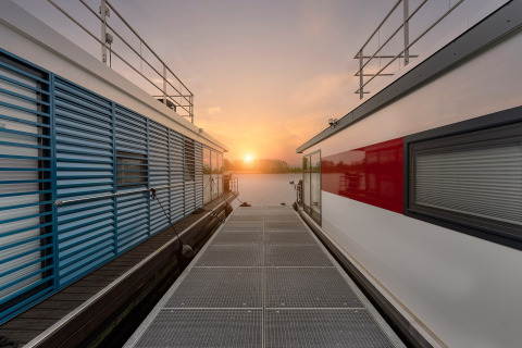 Vista del tramonto tra due moderni houseboat a Zehdenick, lungo il pontile sull’acqua tranquilla.