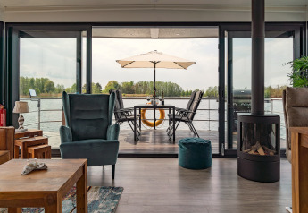 Wohnzimmer auf Hausboot in Zehdenick mit Blick aufs Wasser, große Terrasse mit Esstisch und Sonnenschirm.