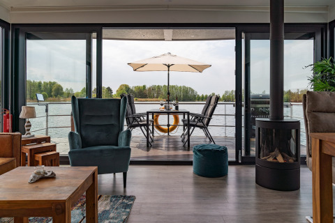 Salón en una casa flotante en Zehdenick con vista al agua, amplia terraza exterior, mesa y sombrilla.