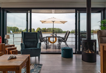 Soggiorno su houseboat a Zehdenick con vista sull’acqua, ampia terrazza, tavolo da pranzo e ombrellone.