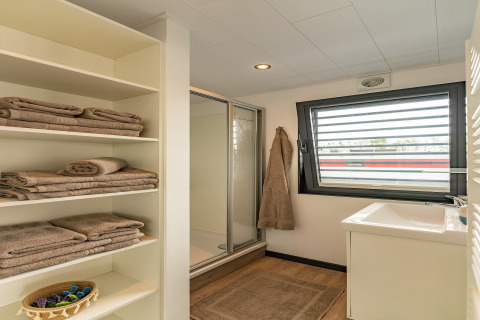 Moderne badeværelse på en husbåd i Zehdenick, Tyskland, med bruseniche, vindue og hylder med håndklæder.