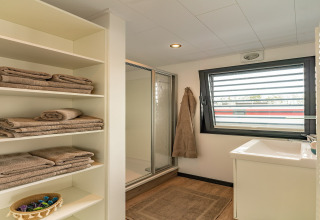 Modern bathroom on a houseboat in Zehdenick, Germany, featuring shower, window, and shelves with towels.