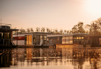 Hausboot «in Zehdenick» auf ruhigem Wasser bei Sonnenuntergang, umgeben von Natur in Deutschland.
