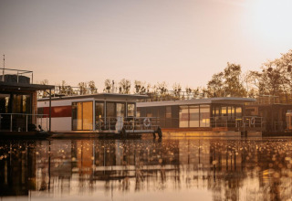 Houseboat «in Zehdenick» floats on calm water at sunset, surrounded by nature in Germany.