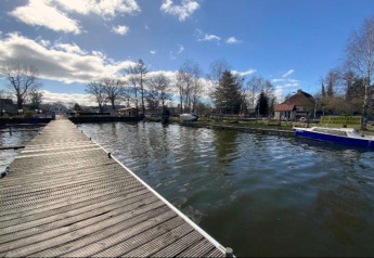 Houten steiger over water met woonboot en huizen op de achtergrond in Zehdenick, Duitsland.