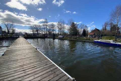 Wooden pier over the water with a houseboat and houses in the background in Zehdenick, Germany.