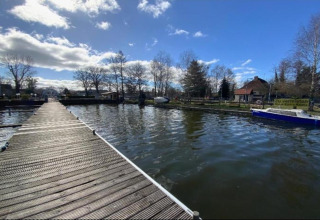 Wooden pier over the water with a houseboat and houses in the background in Zehdenick, Germany.