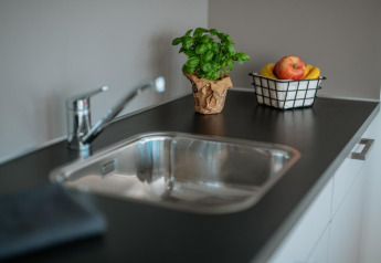 Fregadero de cocina con encimera negra, planta de albahaca y cesta de frutas en una casa flotante en Zehdenick, Alemania.